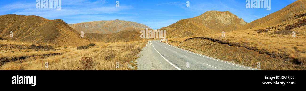 A panoramic view of the Lindis Pass in the South Island of New Zealand. The hills are covered in snow tussocks Stock Photo