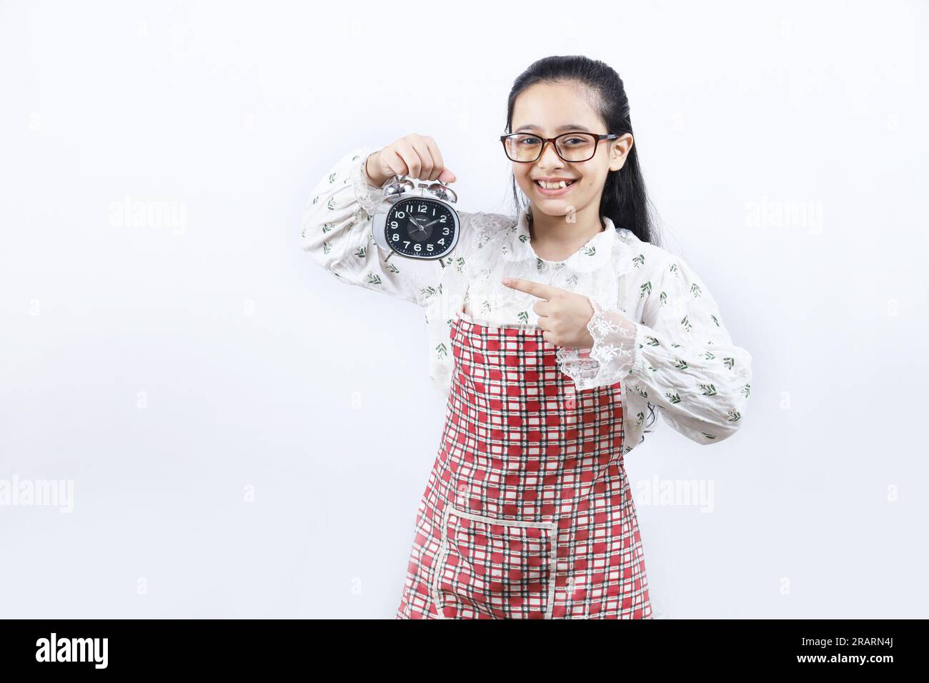 Young teenage girl holding an alarm clock in hand and pointing towards the alarm clock. Stock Photo