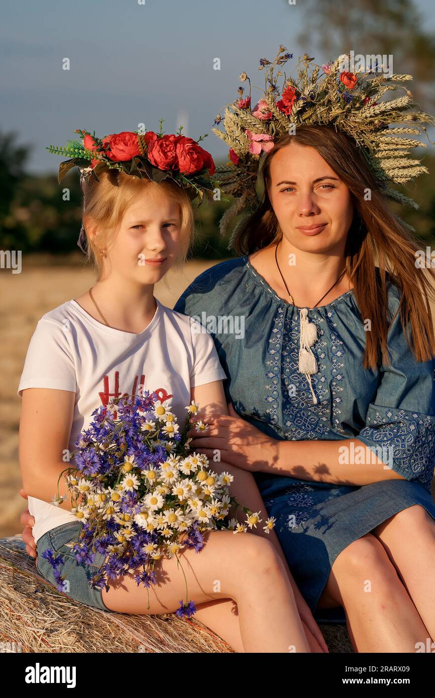 Portrait of mother and daughter in Ukrainian traditional outfits, with wreaths on her head. Constitution day. Patriotic holiday. Woman and child. Stock Photo