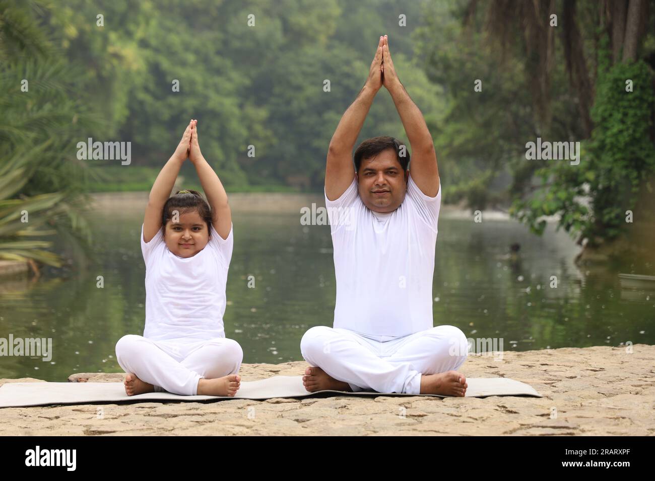Obese family exercising and doing Yoga poses in green serene environment early morning in park to maintain healthy lifestyle. International yoga day. Stock Photo