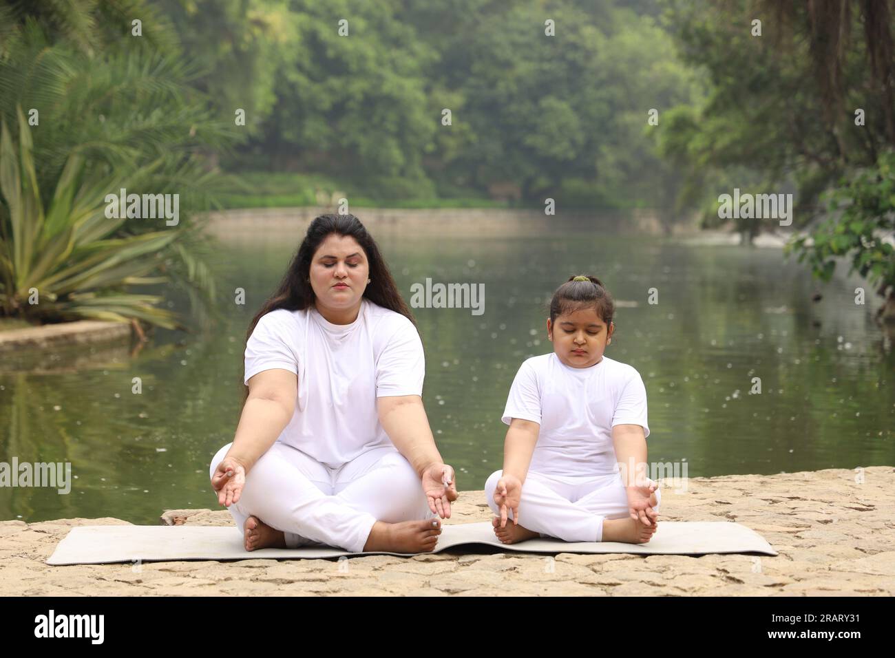 Obese family exercising and doing Yoga poses in green serene environment early morning in park to maintain healthy lifestyle. International yoga day. Stock Photo