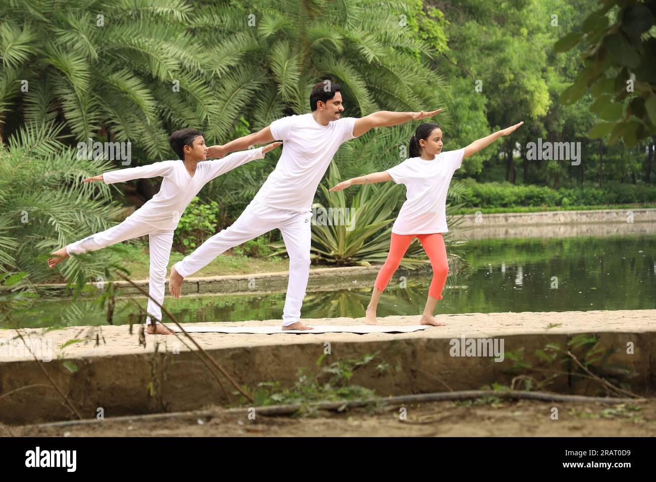 Trainer exercising and teaching kids the yoga poses in green environment early morning in park to maintain healthy lifestyle. International yoga day. Stock Photo