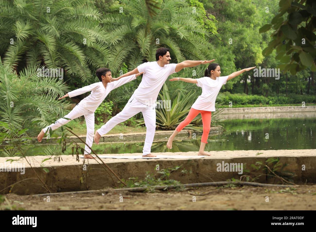 Trainer exercising and teaching kids the yoga poses in green environment early morning in park to maintain healthy lifestyle. International yoga day. Stock Photo