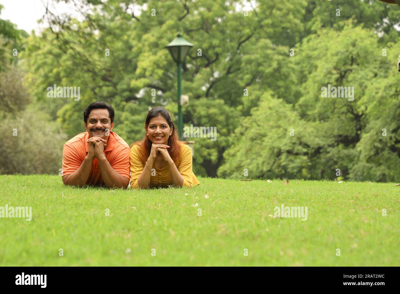 Happy newly married couple sitting together on grass and enjoying their family time early morning. The family is looking at camera. Stock Photo