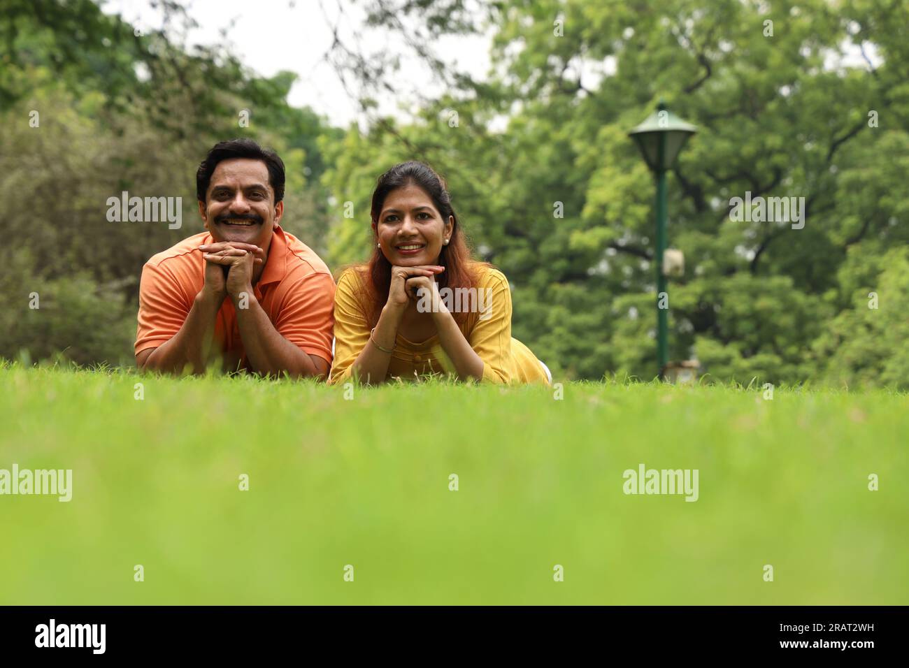 Happy newly married couple sitting together on grass and enjoying their family time early morning. The family is looking at camera. Stock Photo