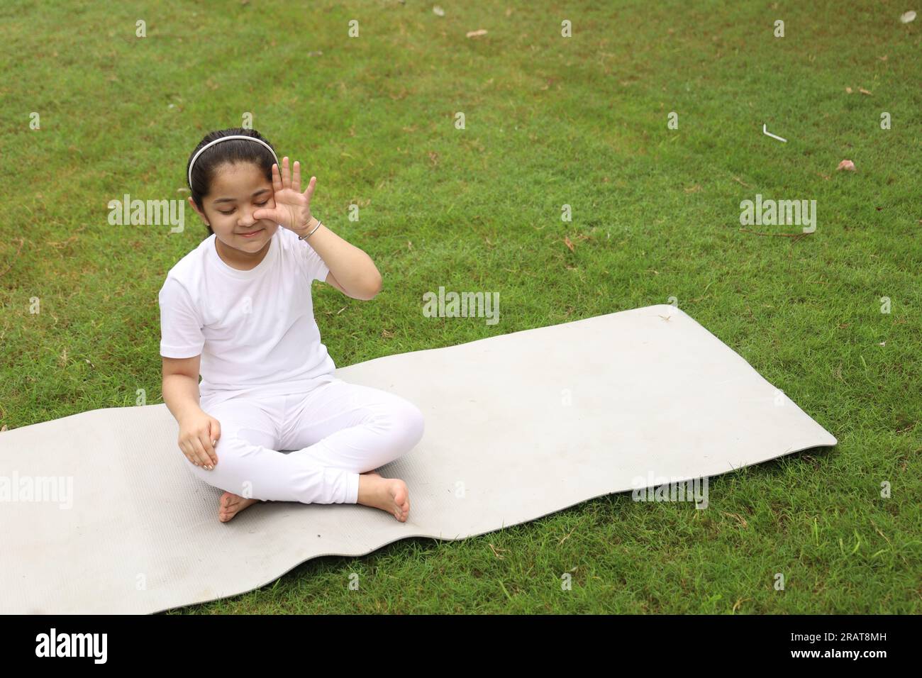 Young kid doing yoga exercises early morning in a green public park. We can see ducks around. The child is health conscious. Happy girl yoga. Stock Photo