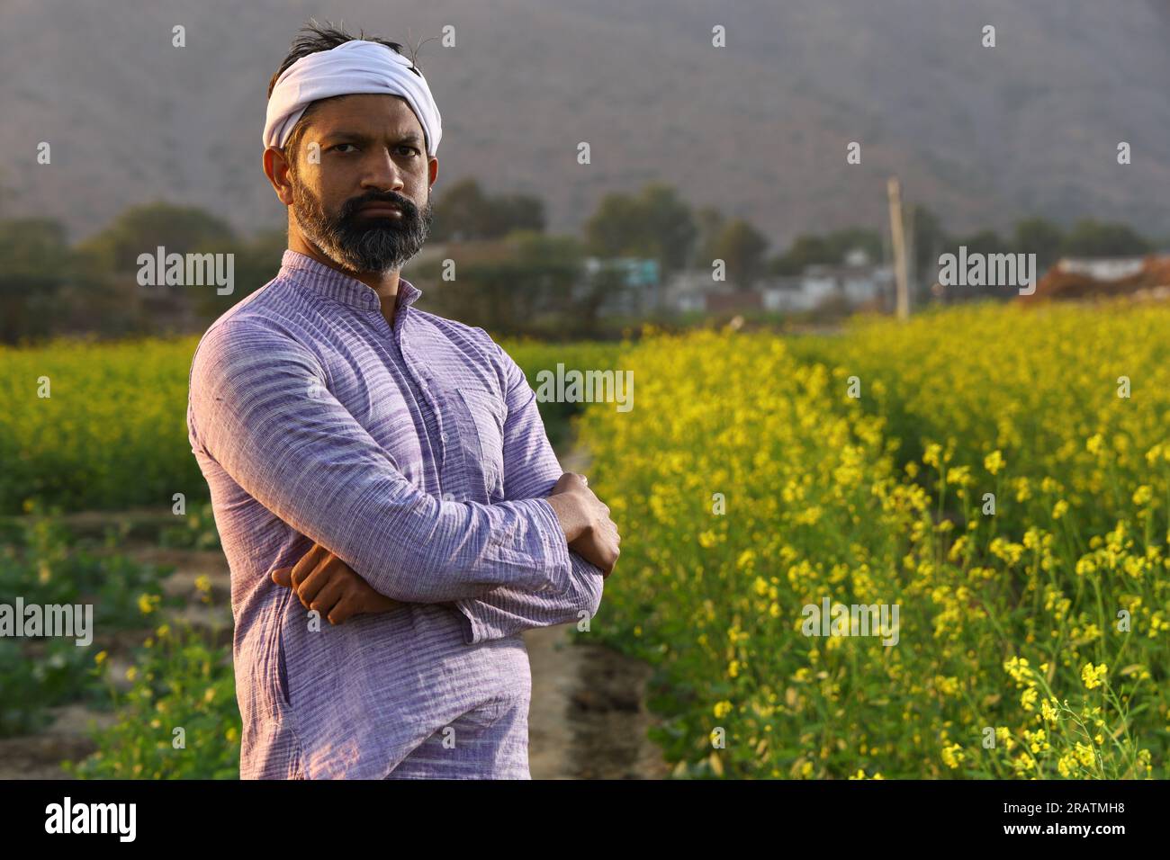 Farmer feeling proud of his effort that he did for growth of his field. Beautiful portrait of Indian rural happy farmer standing in mustard field. Stock Photo