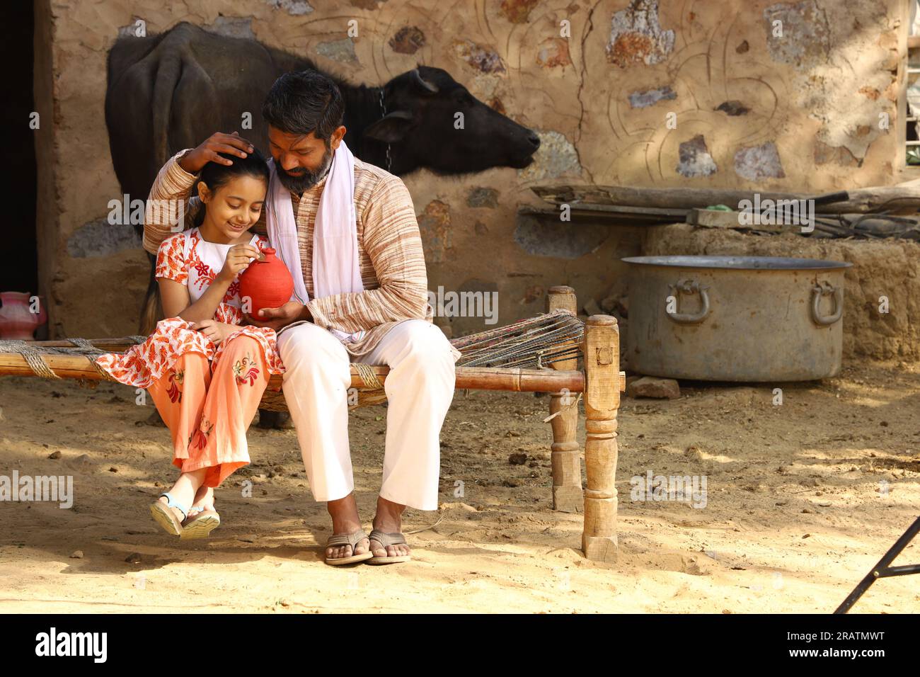 Single father and daughter sitting on folding bed in outdoors holding a piggy bank. Father teaching his daughter the benefits of saving money. Stock Photo