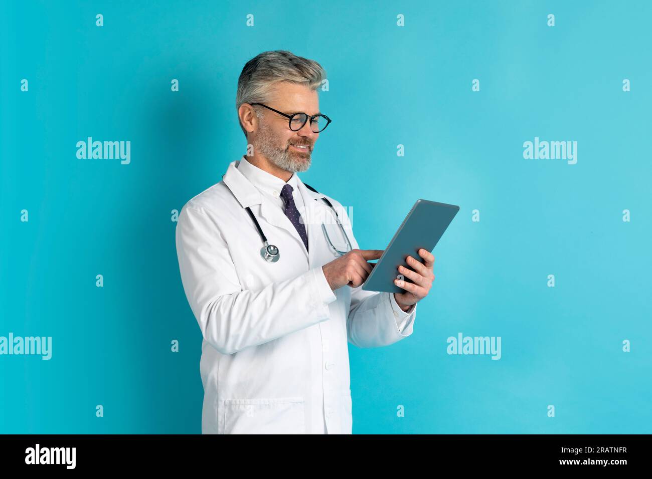 Happy middle aged doctor using digital tablet, blue background Stock Photo