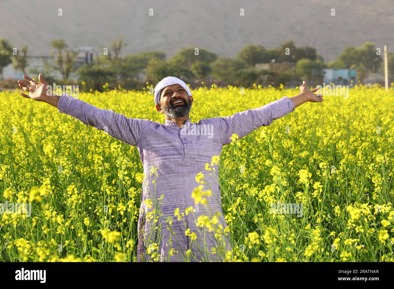 Portrait of Happy Indian farmer feeling the wind while standing in field stretching his arms. Rural India. Joyful Villager to see flourished crops. Stock Photo
