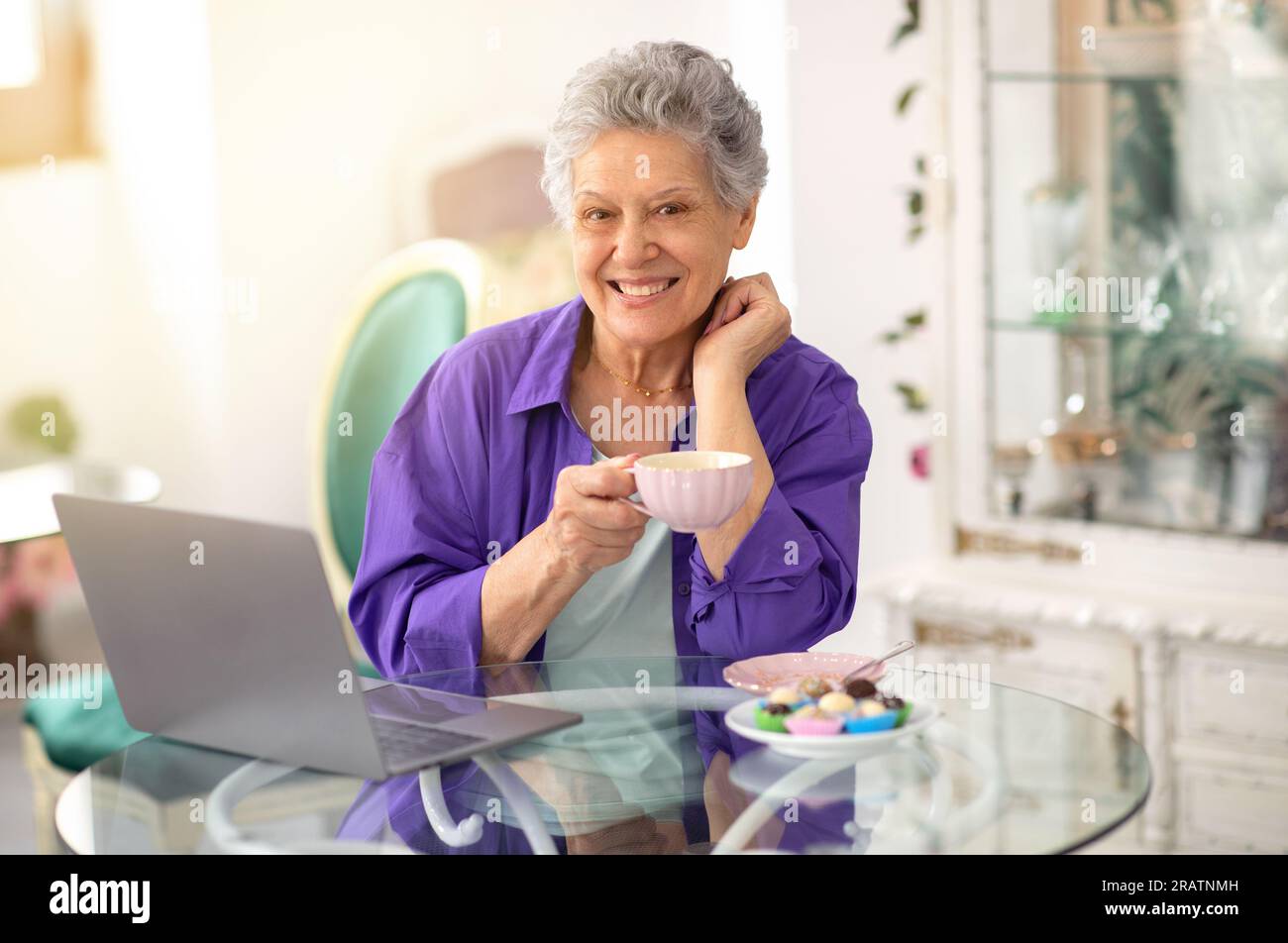 Happy Senior Lady Using Laptop And Having Coffee In Cafe Stock Photo