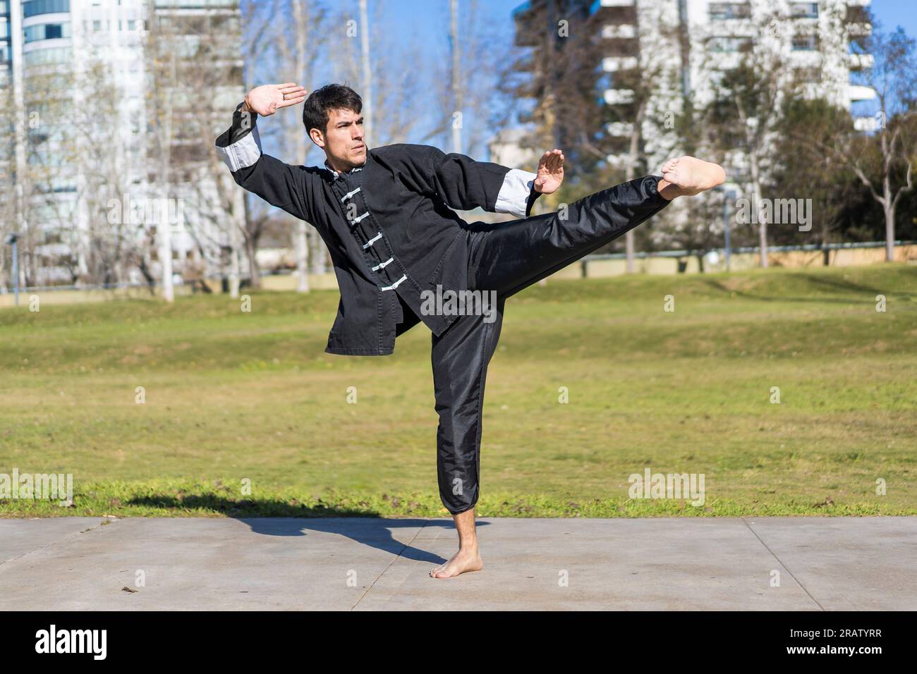 Young athletic martial arts fighter practicing kicks in a public park wearing kung fu uniform. Stock Photo