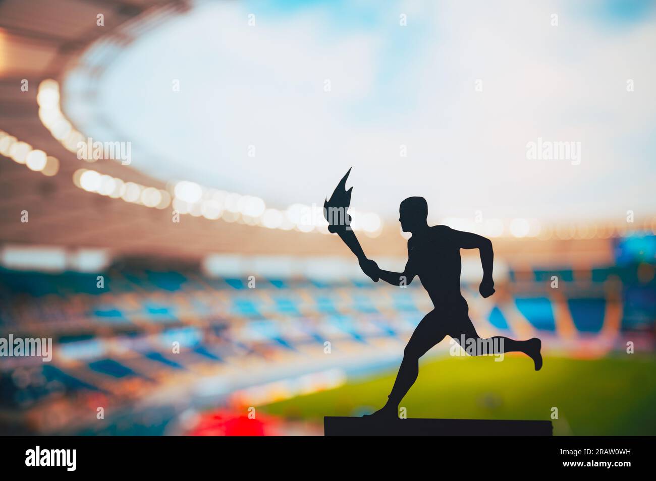 Igniting the Spirit: Silhouette of Male Athlete Carrying the Torch Relay. Modern Track and Field Stadium as the Striking Backdrop. Capturing the Essen Stock Photo