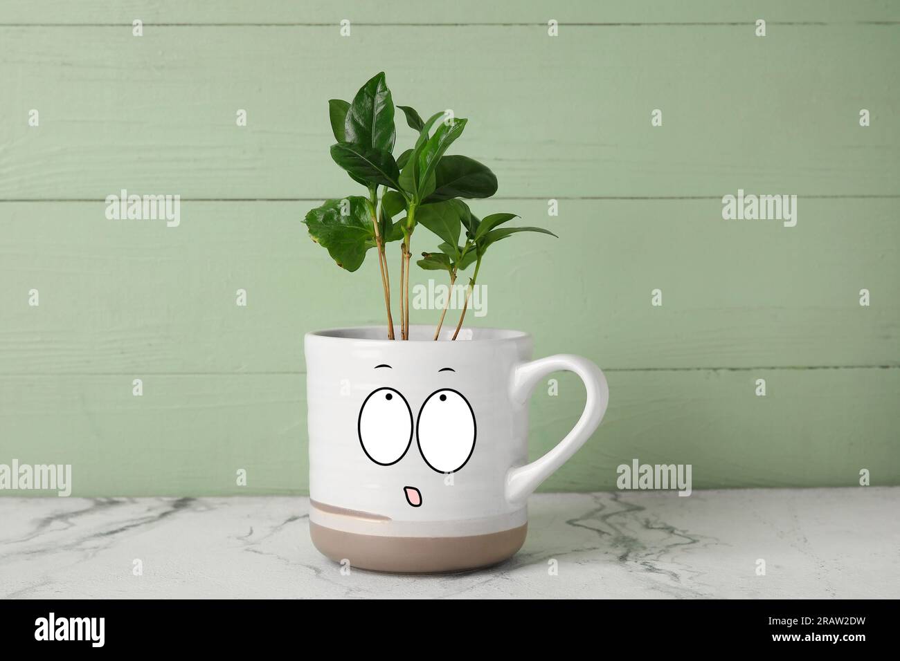 Cup with drawn surprised face and coffee tree on table Stock Photo