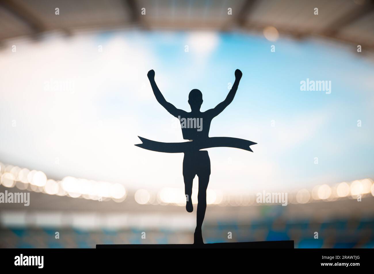 Crossing Boundaries: Runner's Silhouette Breaks the Finish Line Tape at Modern Athletics Stadium. Edit Space, Track and Field Competition Photo. Stock Photo