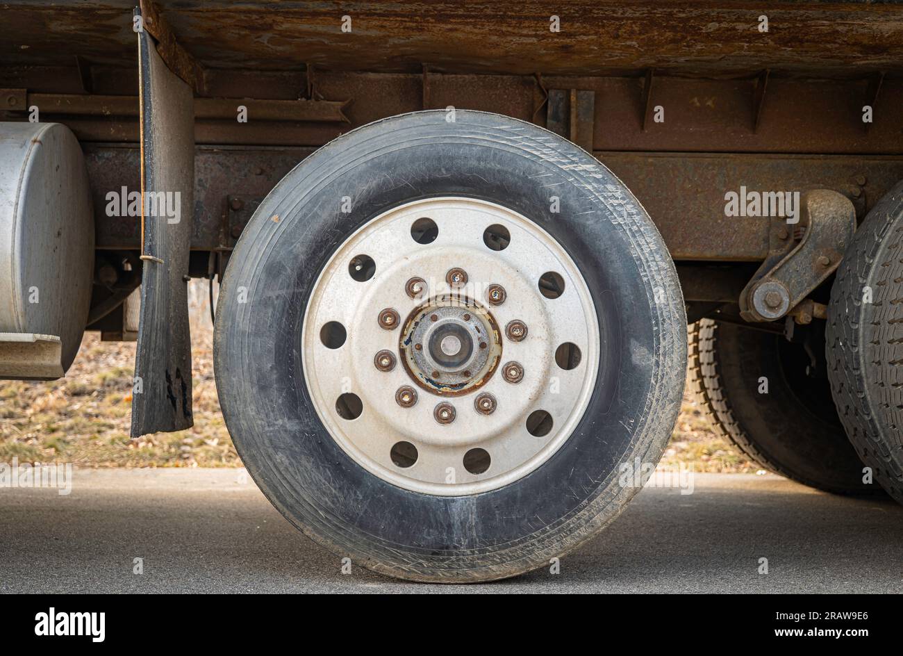 Dusty truck wheel and tire of a truck with round circular pattern. Gas tank and mud flap are also seen. Stock Photo