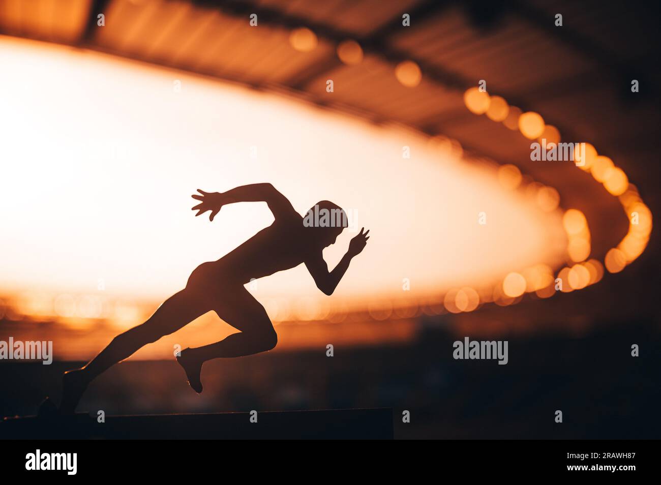 Chasing Glory: Silhouette of an Athlete, Primed for Speed, Standing Tall Amidst the Luminous Dusk at a Modern Sports Stadium. Warm sunset light. Edit Stock Photo