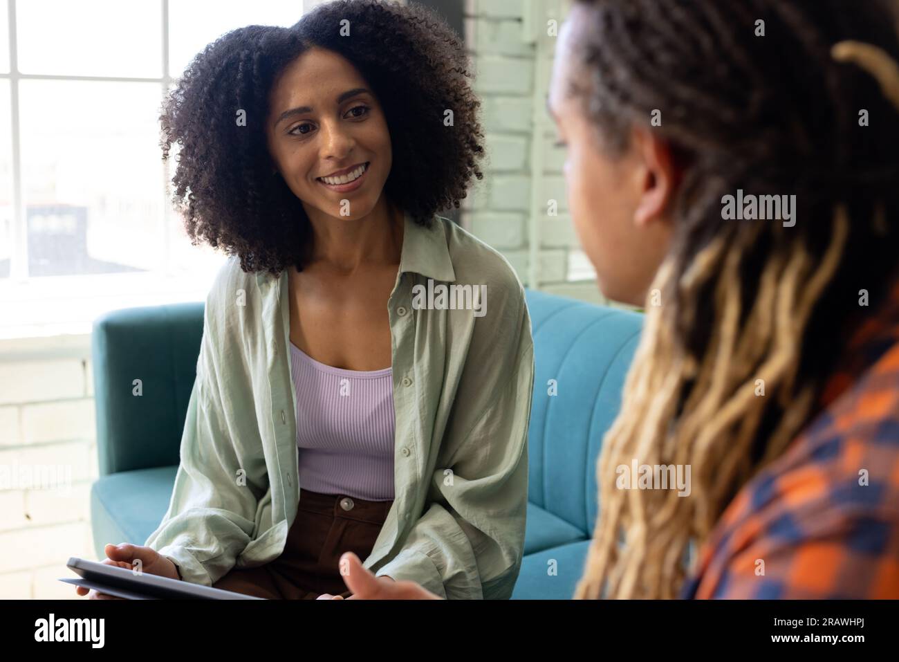 Happy diverse male and female casual business colleagues sitting on sofa talking at office. Business, teamwork and work, unaltered. Stock Photo