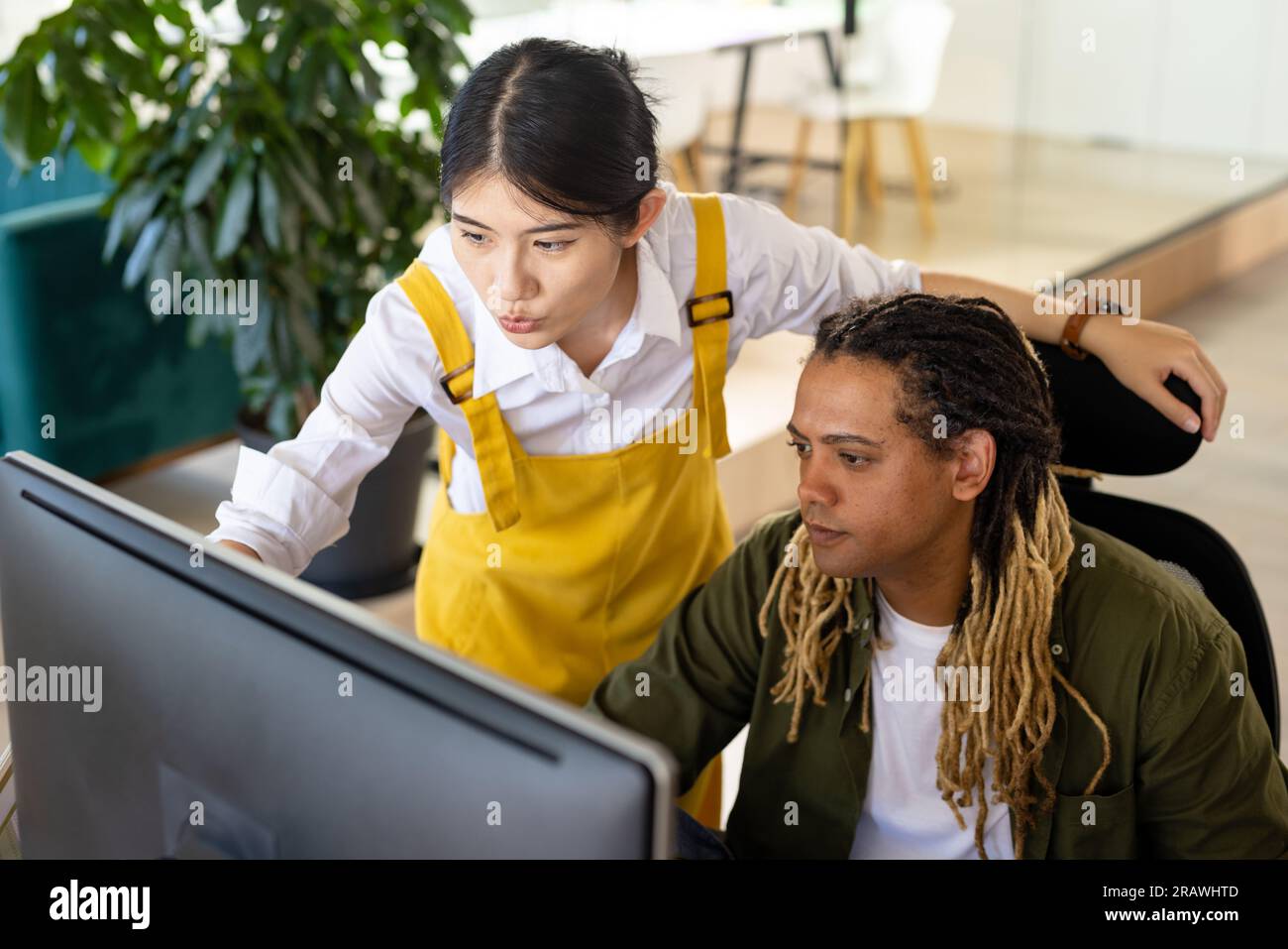Diverse casual business colleagues using computer discussing work at desk in office. Teamwork, work, business, communication and casual office, unalte Stock Photo