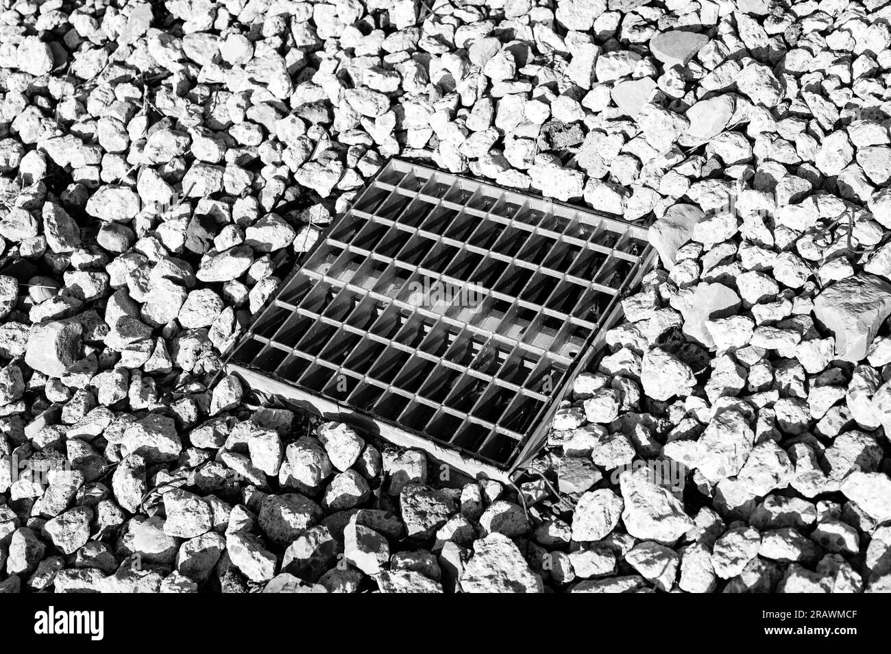 Grated storm drain inlet surrounded by rock for soil erosion control  Stock Photo