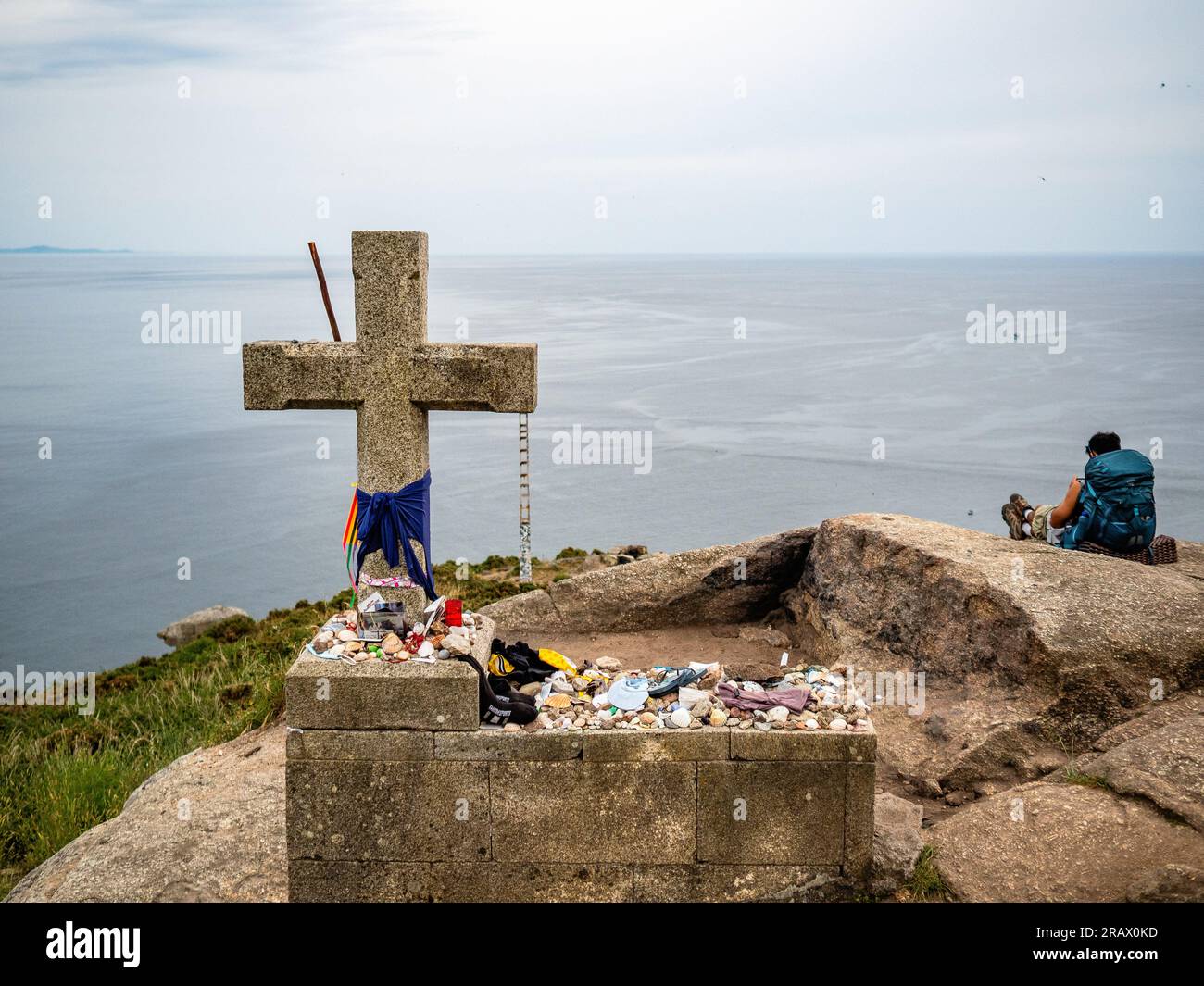 June 6, 2023, Finisterre, Spain: A pilgrim is seen taking a break next to one of the last stone crosses along the route. The Camino de Santiago (the Way of St. James) is a large network of ancient pilgrim routes stretching across Europe and coming together at the tomb of St. James (Santiago in Spanish) in Santiago de Compostela, Spain. Finisterre was both the end of the known world until Columbus altered things and the final destination of many of the pilgrims who made the journey to Santiago in past centuries. Pilgrims in past centuries also continued northwards up the coast to the Santuario Stock Photo