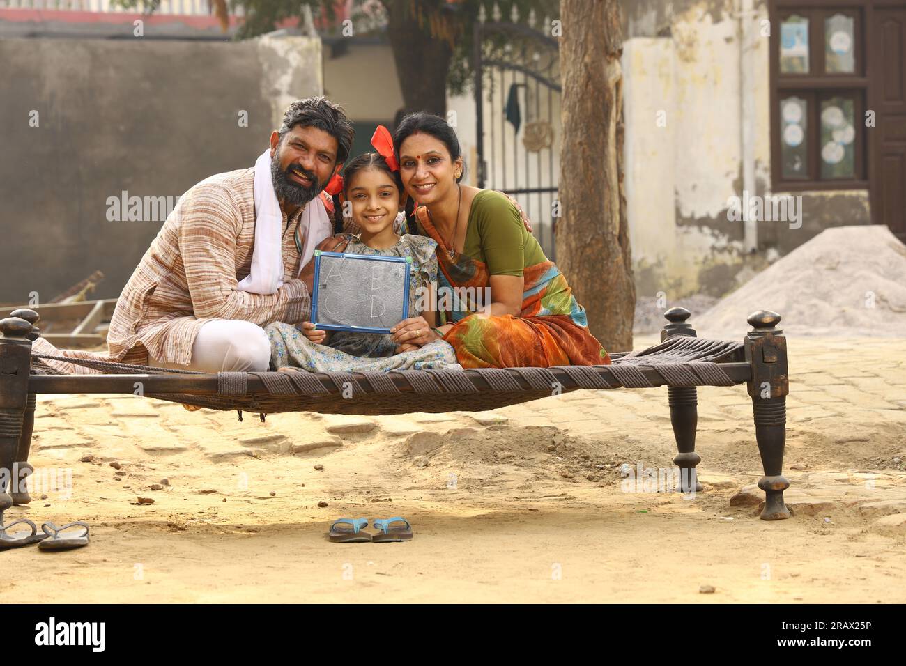 Happy rural Indian family sitting together outside their cottage in day time daughter holding small white board. Literate India. Stock Photo