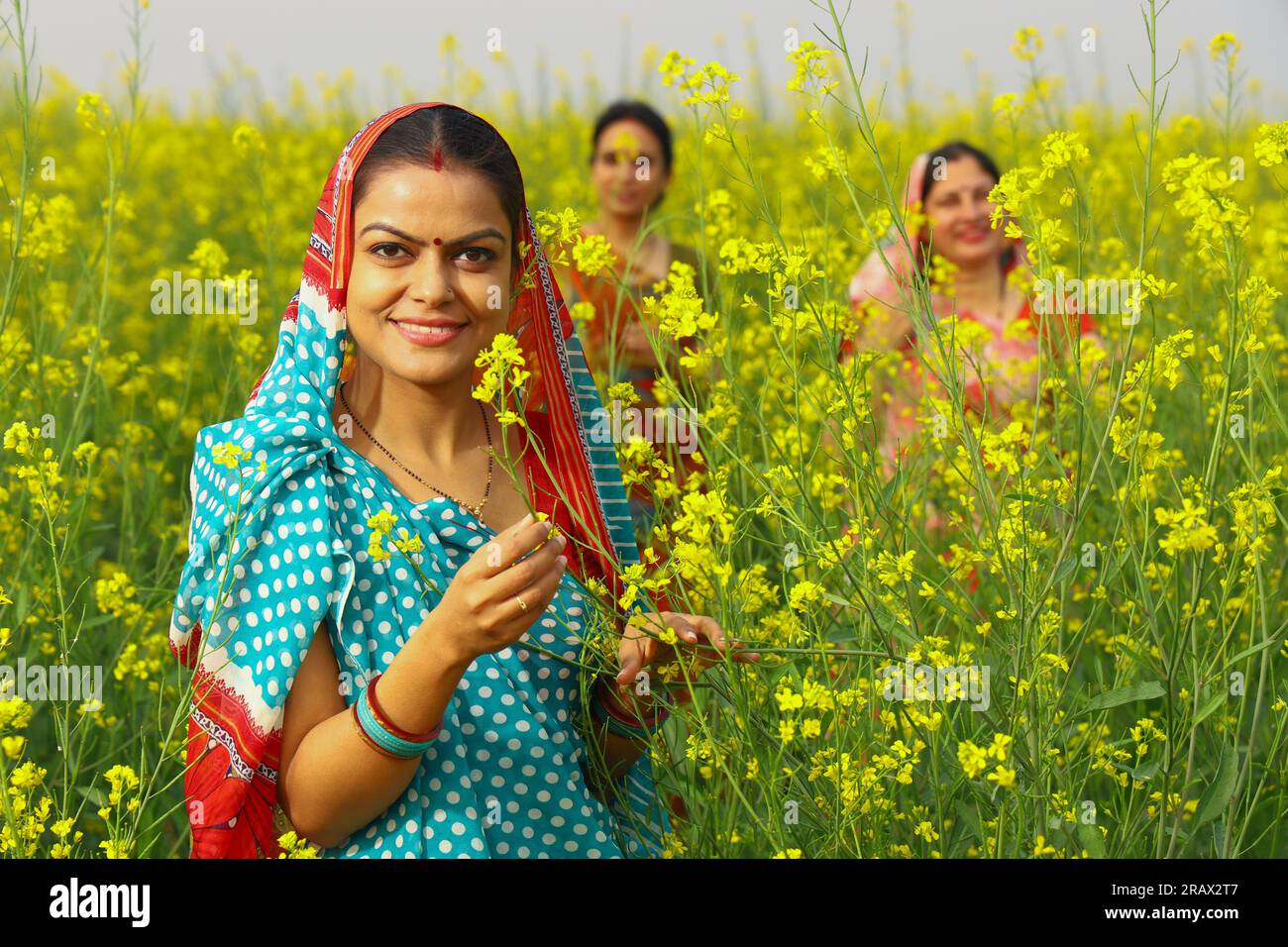 Happy rural Indian women standing in a mustard field enjoying the