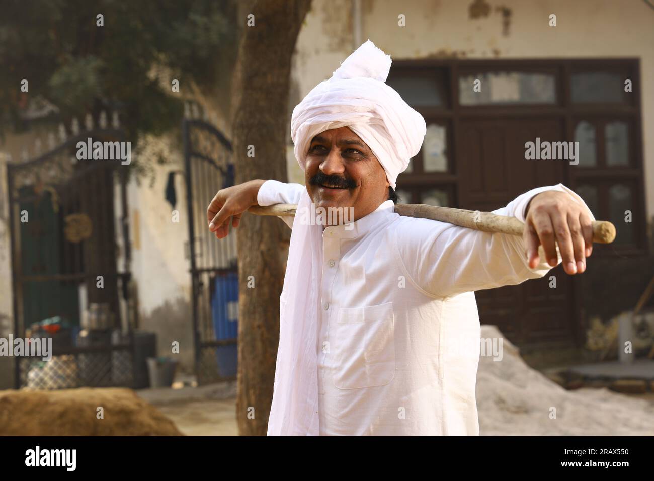 Happy Rural Indian Village man in turban sitting outdoors in a day time.  Holding walking cane. Stock Photo