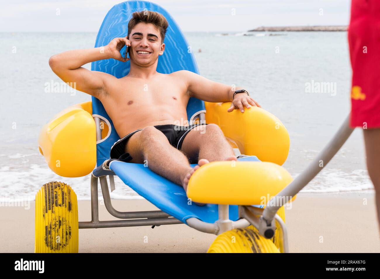 Man rescued on the beach talking with the mobile phone sitting on a floating chair Stock Photo