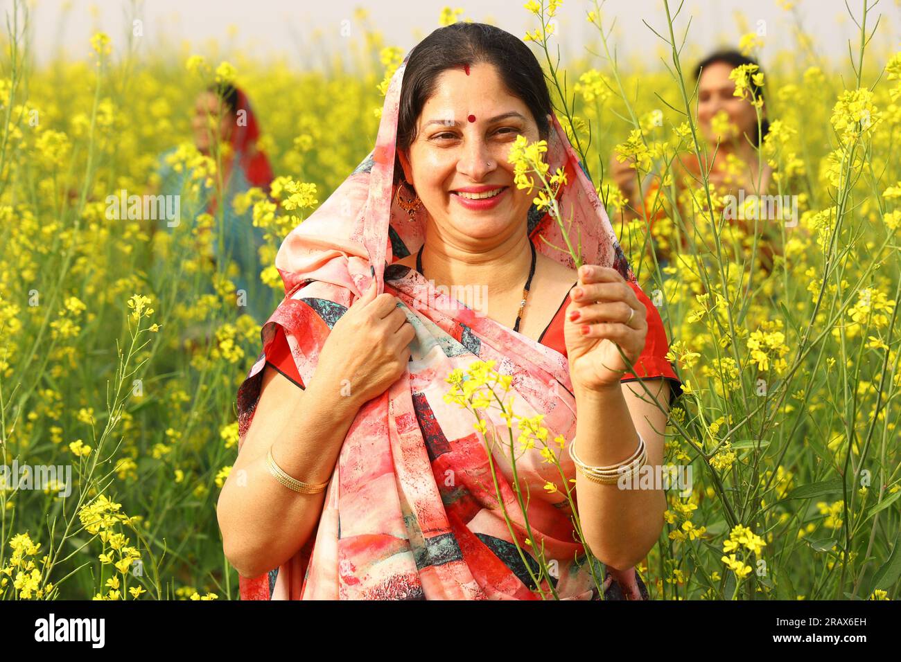 Happy rural Indian women standing in a mustard field enjoying the benefits of the mustard agricultural field. Stock Photo