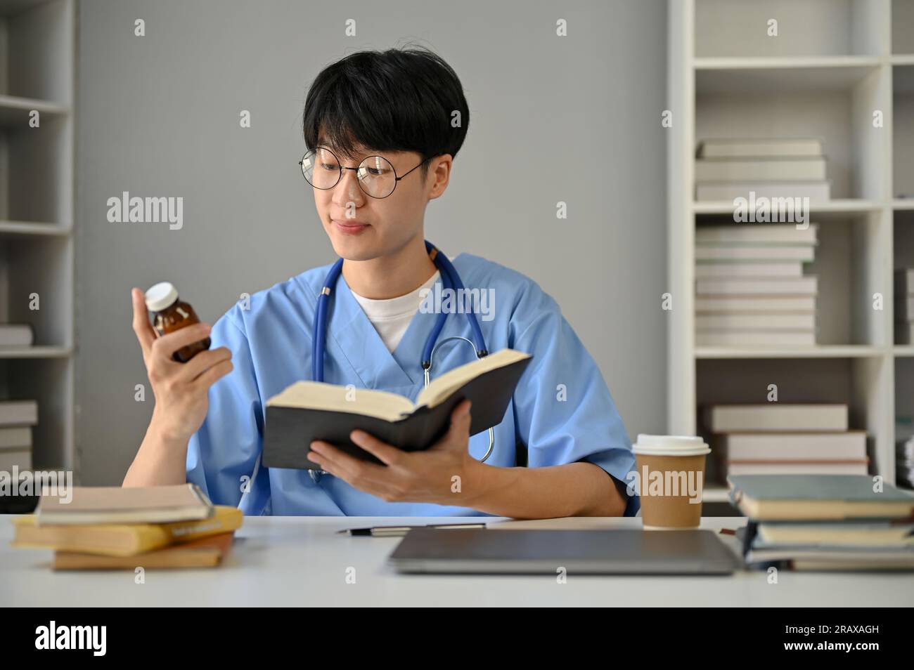 A smart and focused young Asian male medical student in scrubs studying ...