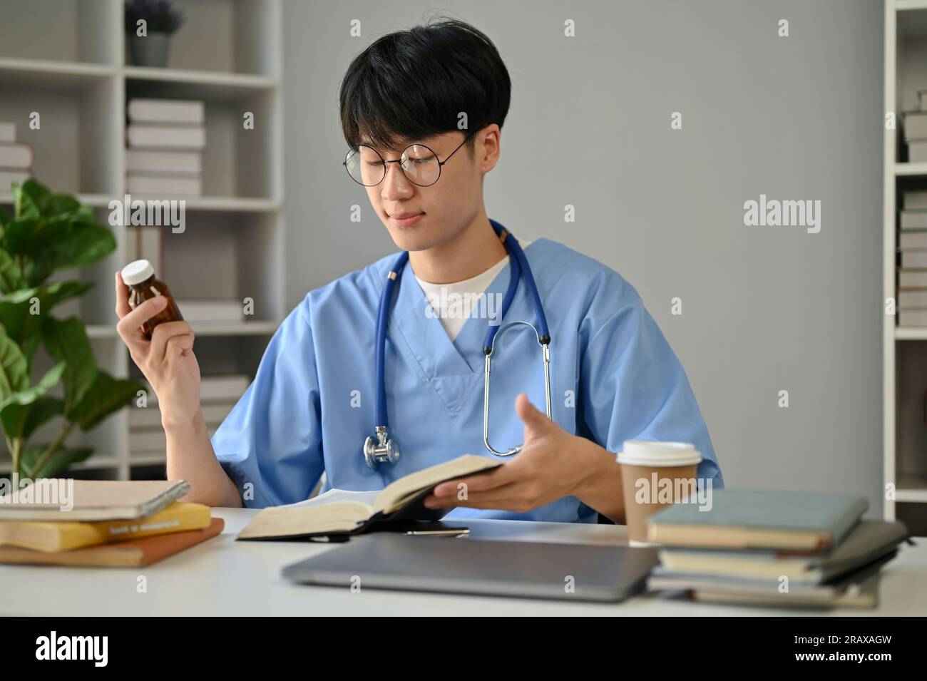 A smart and focused young Asian male medical student in scrubs studying ...