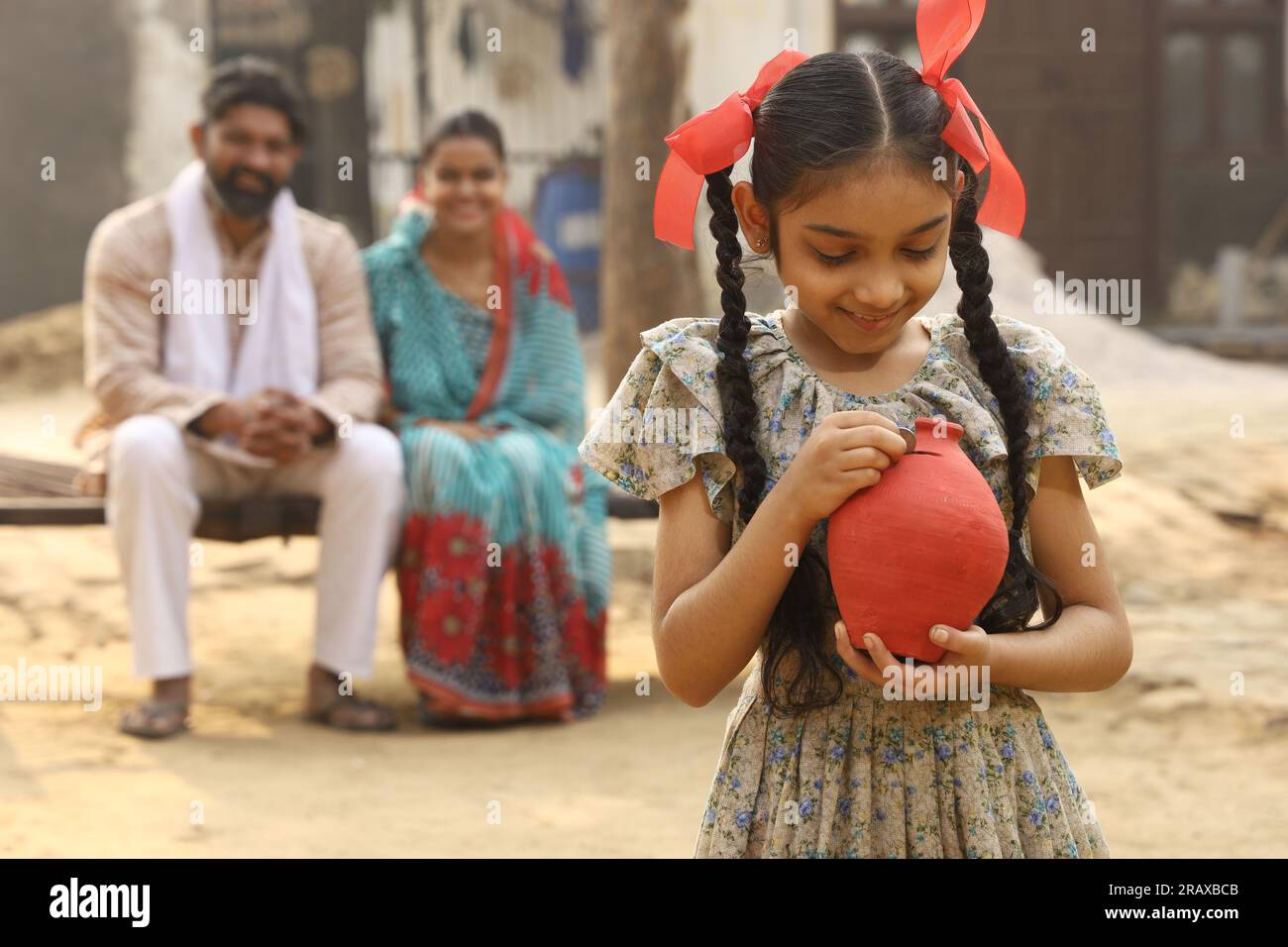 Happy rural Indian family sitting together, daughter is holding a piggy ...