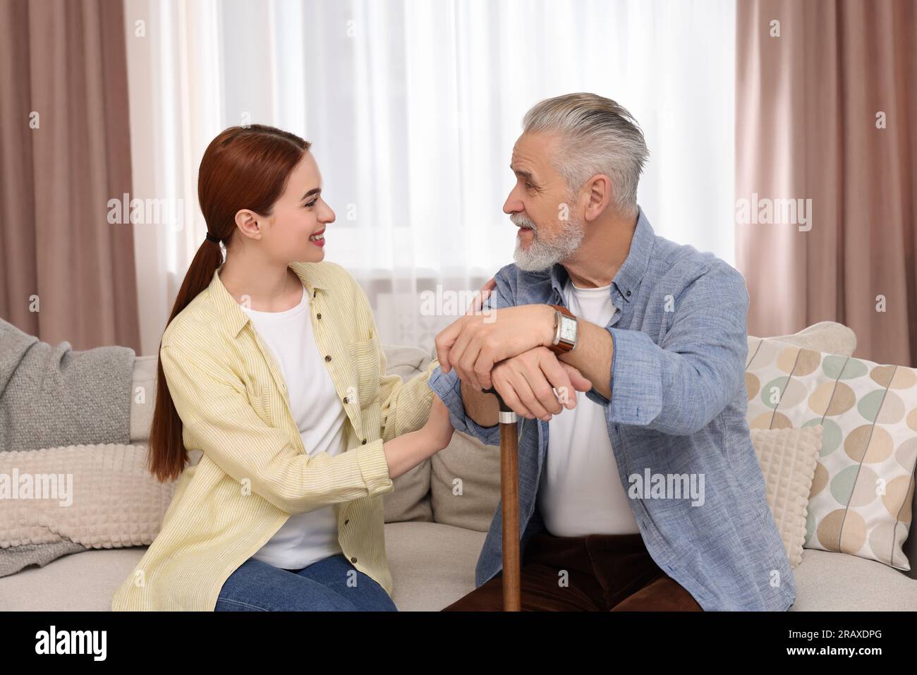 Caregiver and senior man with walking cane on sofa at home Stock Photo ...