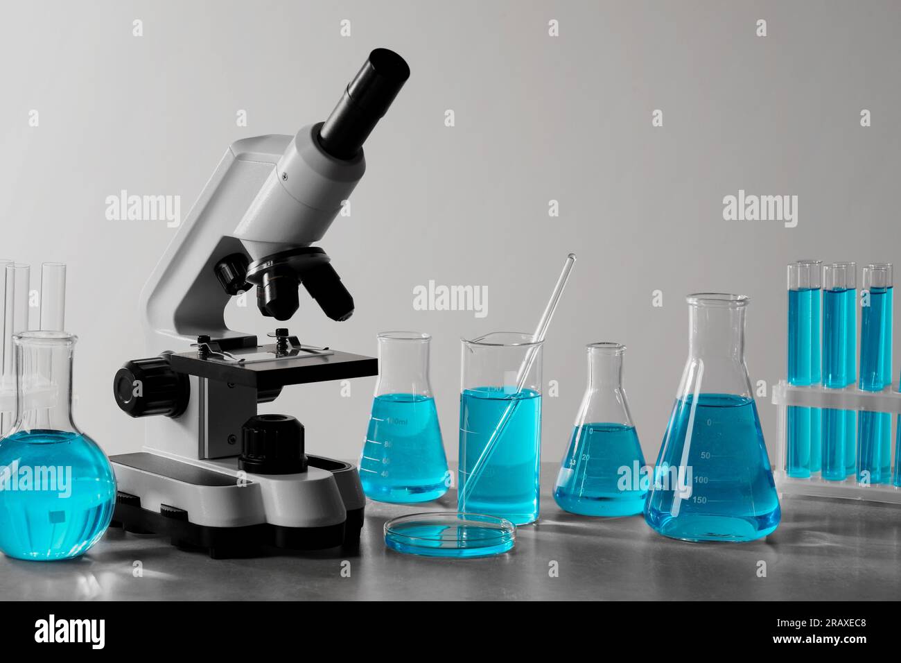 Different laboratory glassware with light blue liquid and microscope on ...
