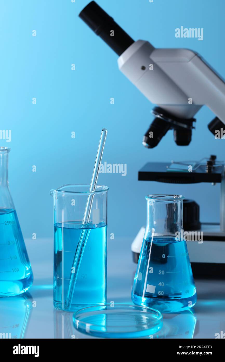 Different laboratory glassware with light blue liquid and microscope on ...