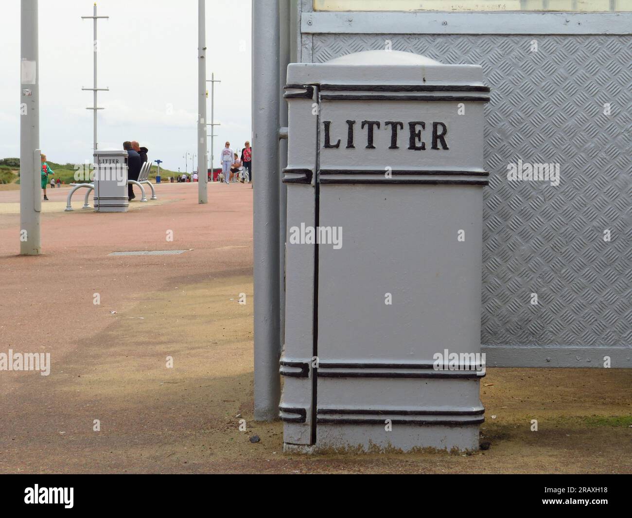 A grey Litter bin on the seafront pavement with people in the distance Stock Photo