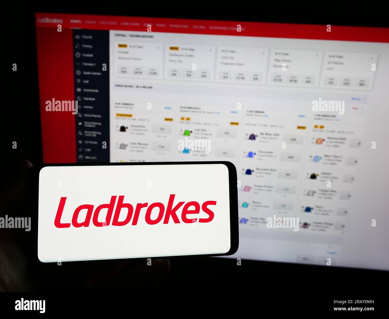 Person holding smartphone with logo of company LC International Limited (Ladbrokes) on screen in front of website. Focus on phone display. Stock Photo