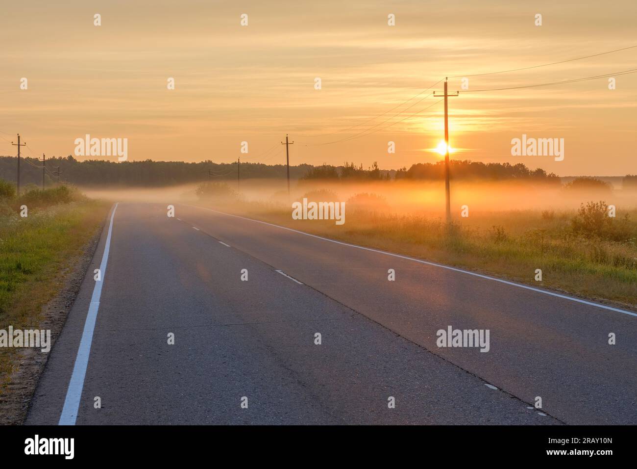 Rising sun and fog over an empty suburban highway on a summer morning ...