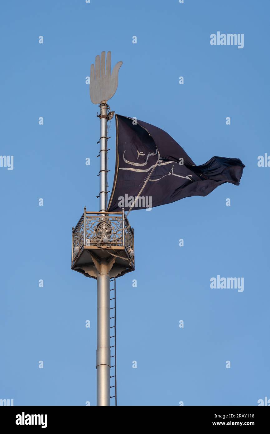 Bhit Shah, Sindh, Pakistan - 11 16 2019 : Black shia muslim flag on a mast with silver hamsa on blue sky background, Shah Abdul Latif Bhittai shrine Stock Photo