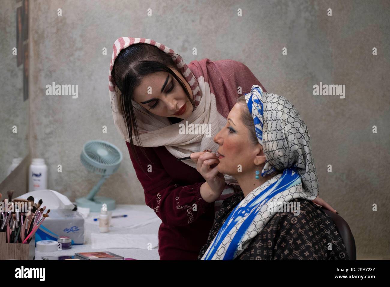 A female Iranian makeup artist is applying makeup to Iranian actress