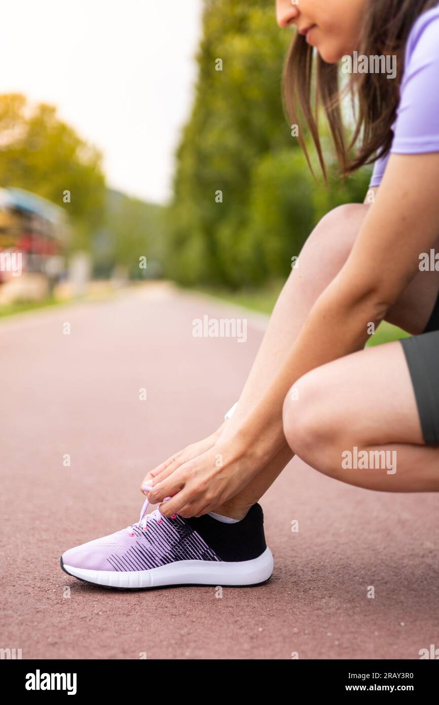 Sport woman tying running shoe laces during fitness training outdoors. Young female athlete running workout. Wellness, exercise and healthy lifestyle. Stock Photo
