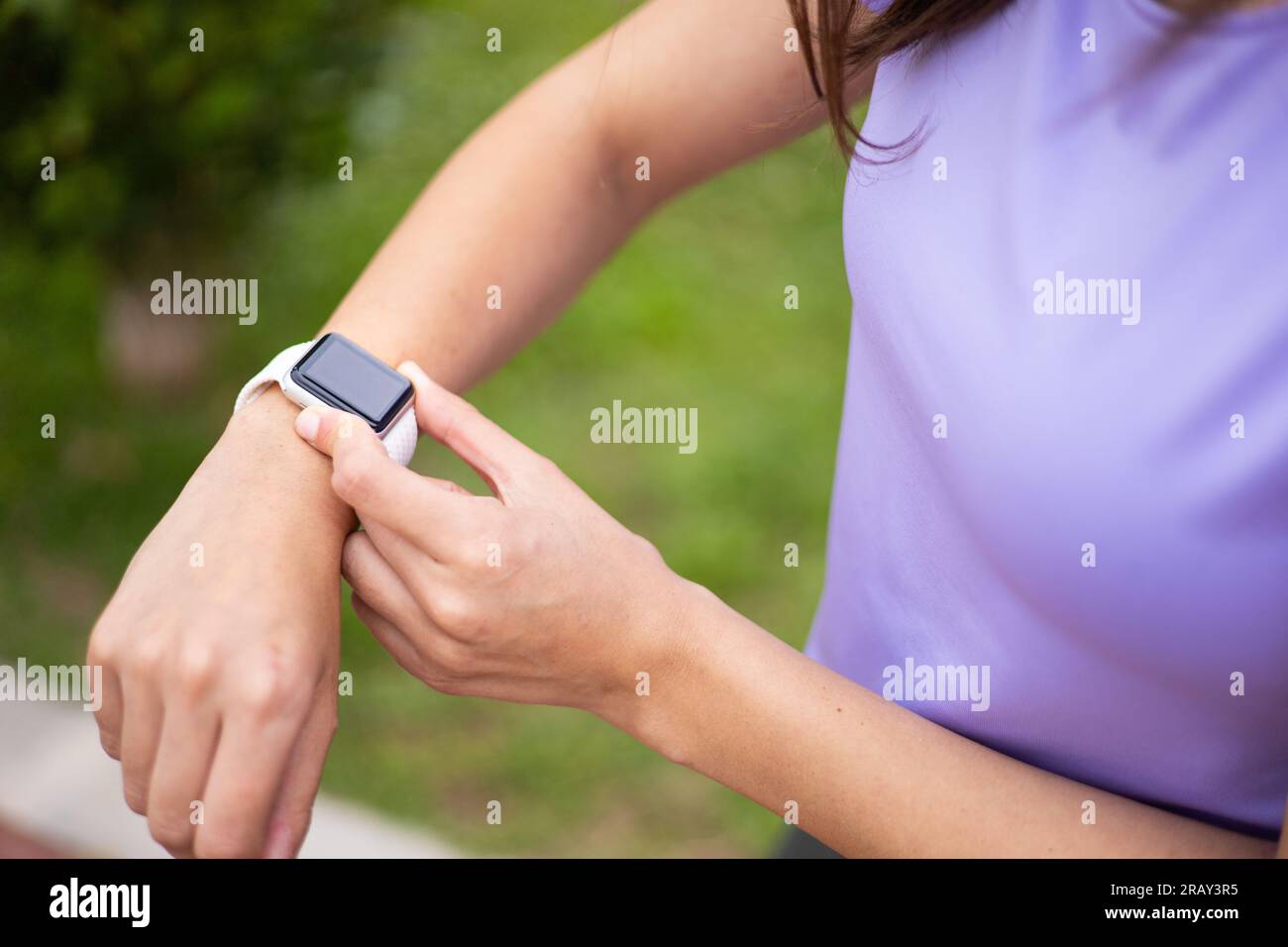 Young woman checking a sport smartwatch after running outdoors. Female with fitness tracker watch to monitor training in an urban park. Stock Photo