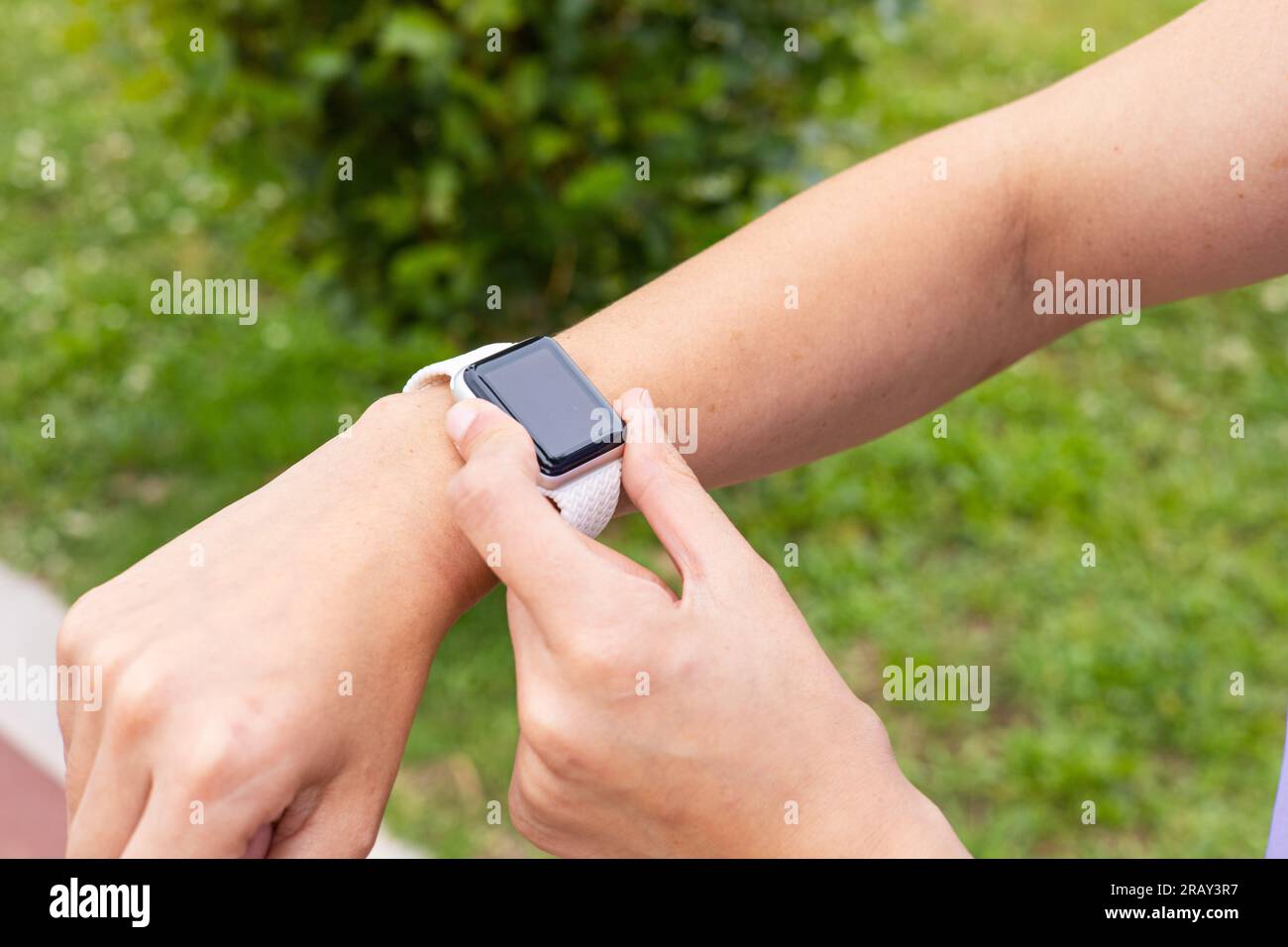 Young woman checking a sport smartwatch after running outdoors. Female with fitness tracker watch to monitor training in an urban park. Stock Photo