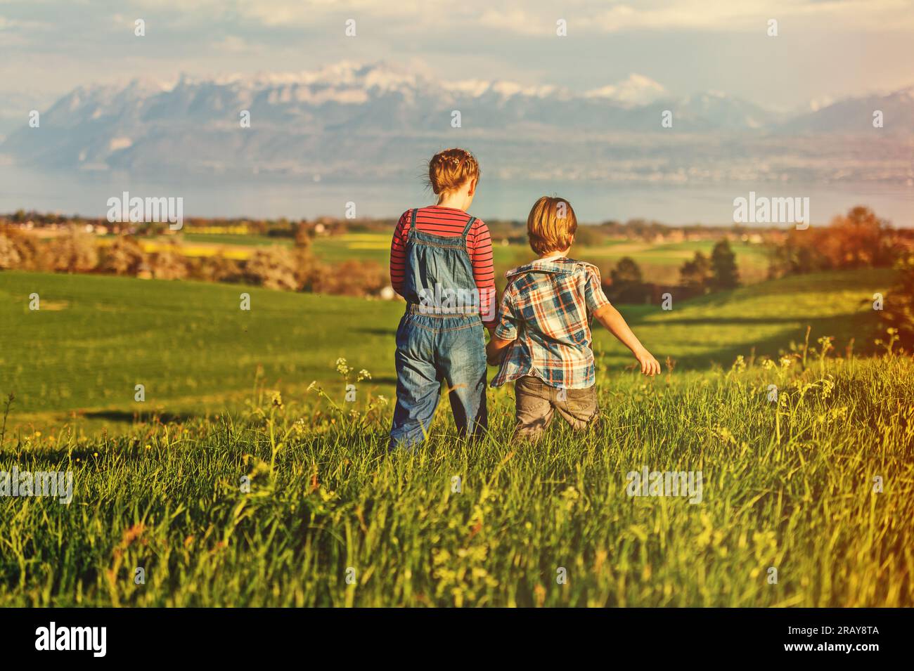 Two kids, little brother and big sister, playing together outdoors in swiss fields with view on