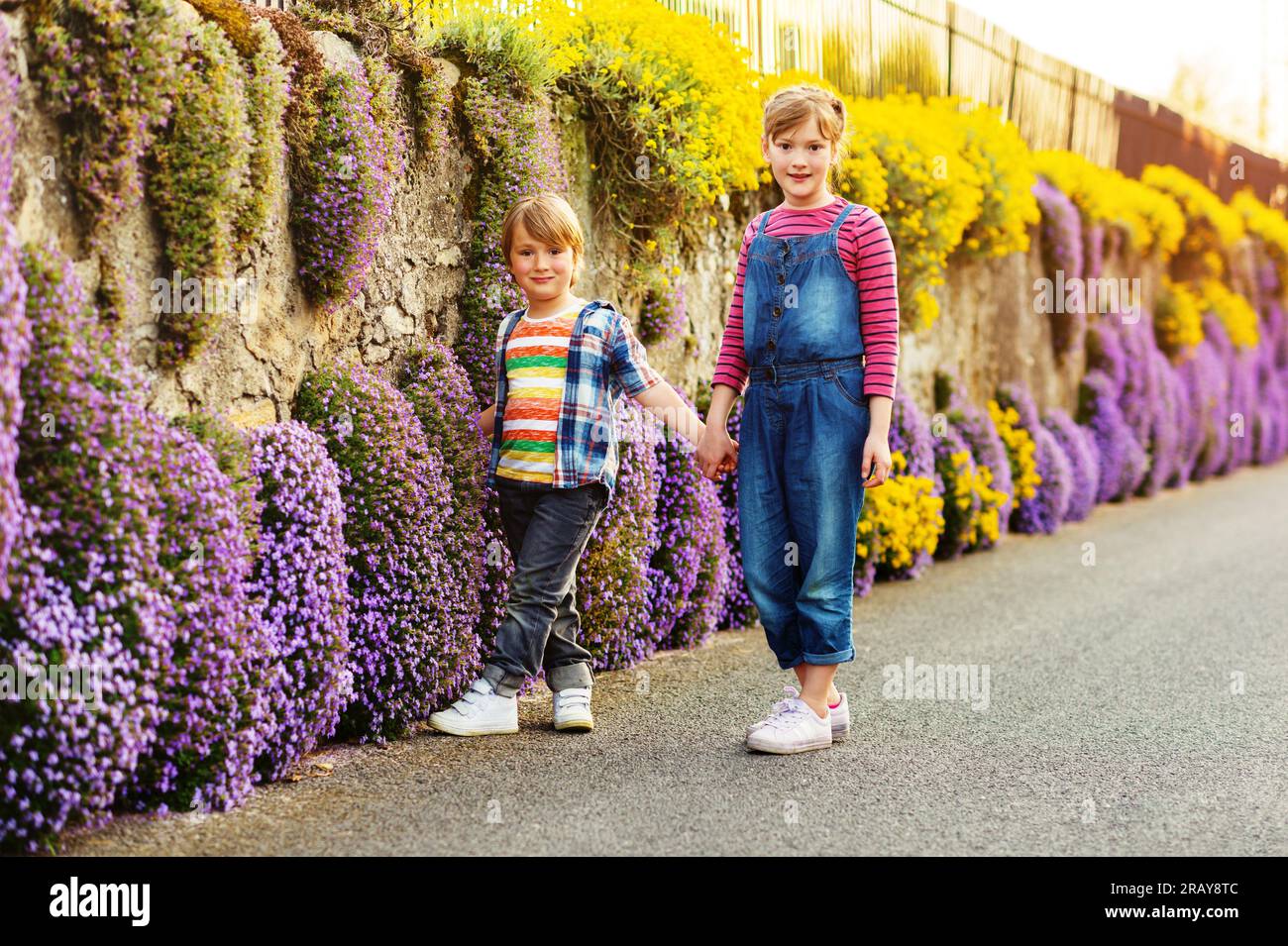 Two cute happy young kids playing together outdoors on a nice sunny evening, holding hands. Small brother and big sister spending time together. Stock Photo