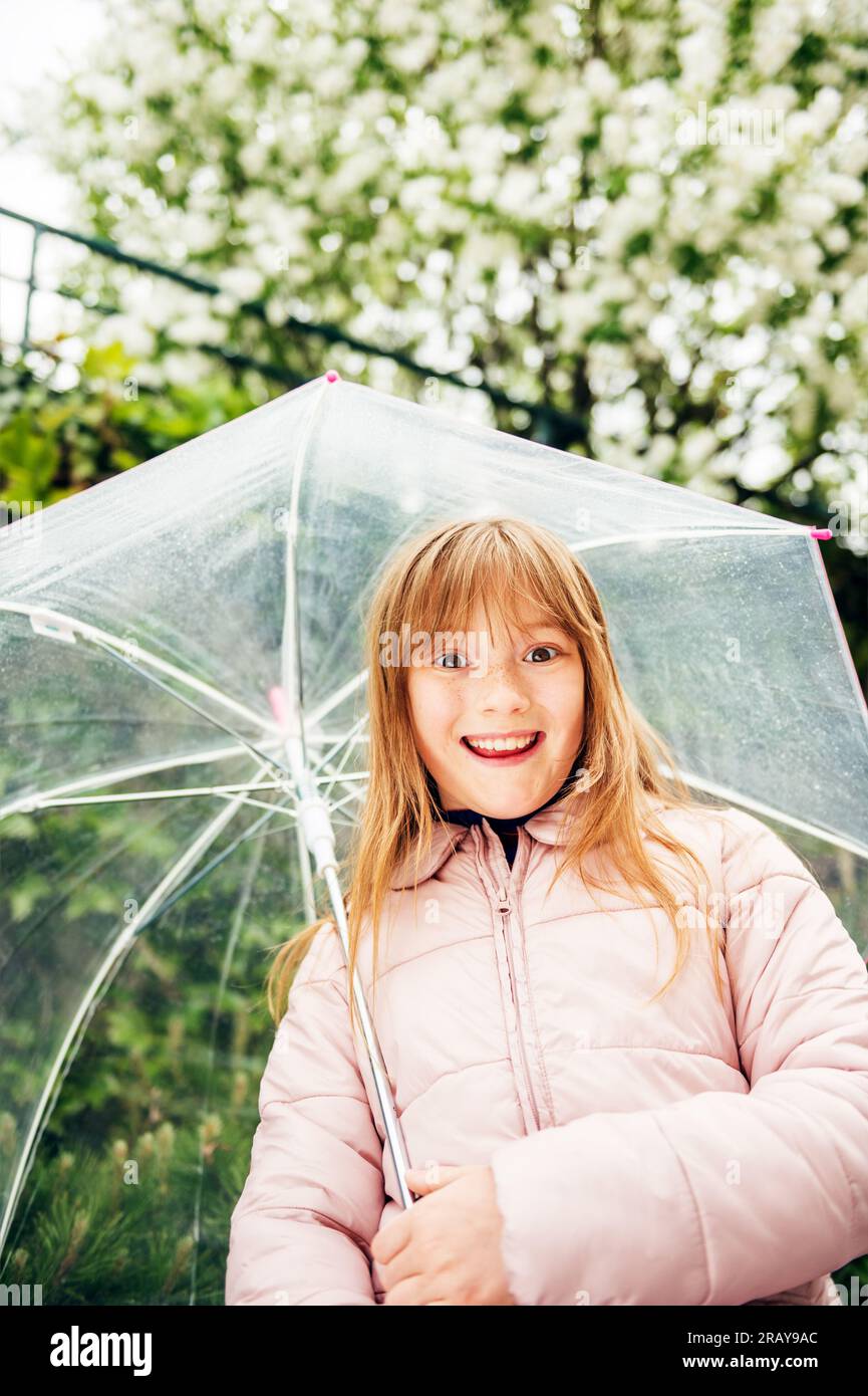 Happy kid girl playing under the rain, holding transparent umbrella Stock Photo