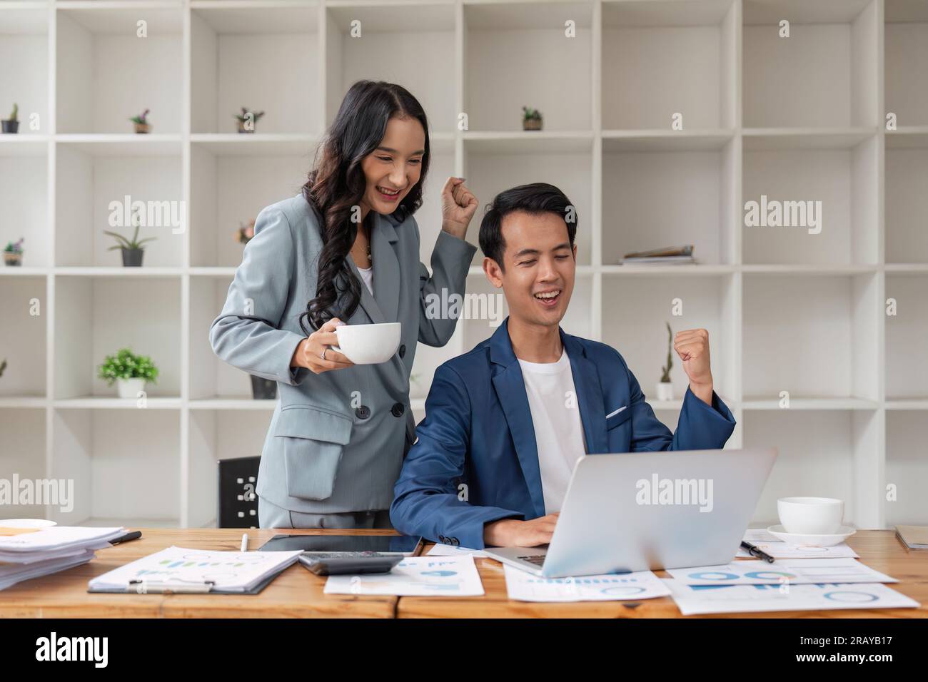 Two asian business people successful excited raised hands rejoicing with a laptop computer in office Stock Photo