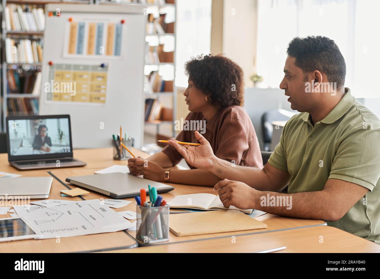 Migrant students having online lesson with teacher while sitting at table and studying foreign language Stock Photo