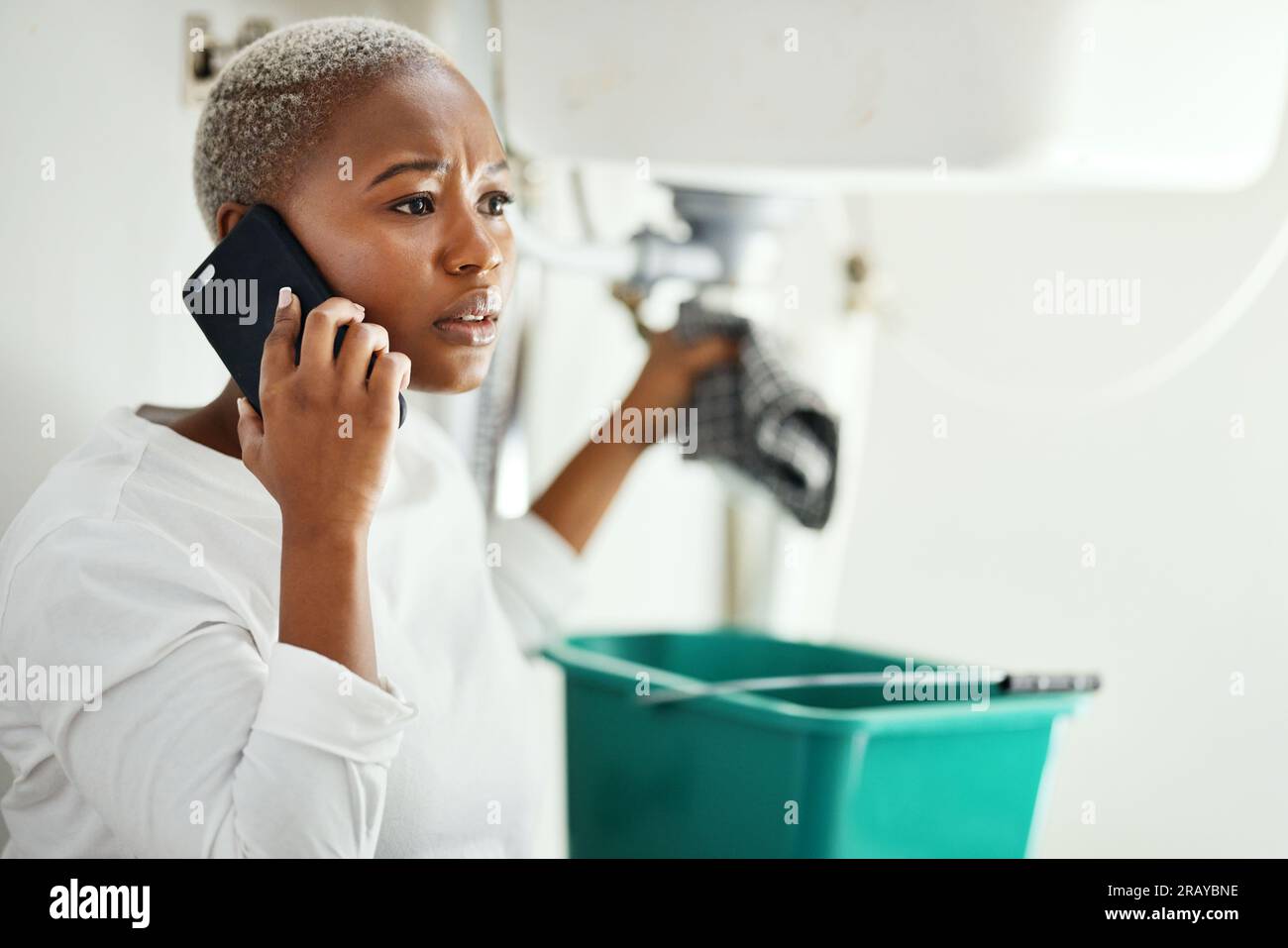 Phone call for plumbing service, woman in bathroom and help from expert contractor to fix leak. Stress, African person on cellphone and problem with Stock Photo